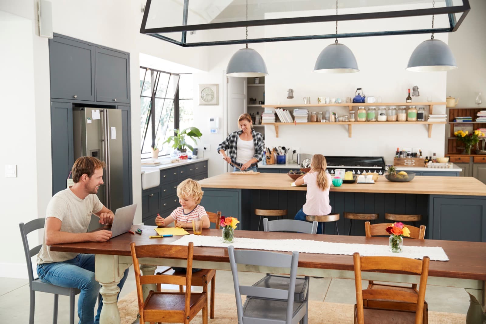 A family at the kitchen table in their finished home, one child drawing while dinner is made